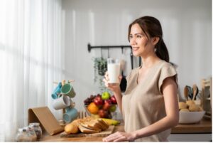 Femme souriante tenant un verre de lait en cuisine.
