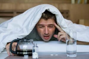Homme fatigué reprenant sa cafetière sous la couette.